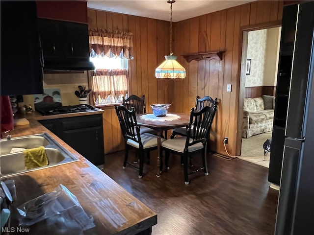 kitchen featuring dark wood-type flooring, premium range hood, stainless steel gas cooktop, wood walls, and sink