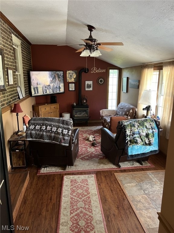 bedroom with lofted ceiling, a wood stove, ceiling fan, brick wall, and hardwood / wood-style flooring