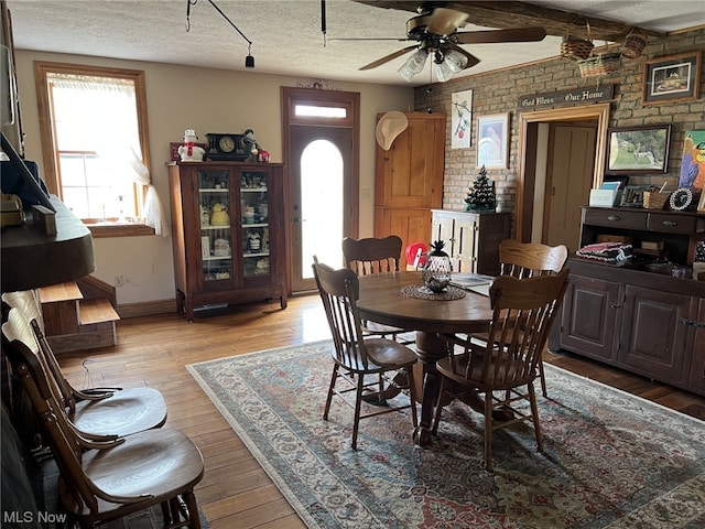 dining area featuring a textured ceiling, wood-type flooring, brick wall, and ceiling fan