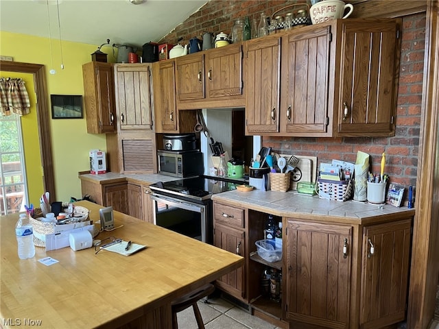 kitchen featuring brick wall, tile counters, vaulted ceiling, and stainless steel appliances