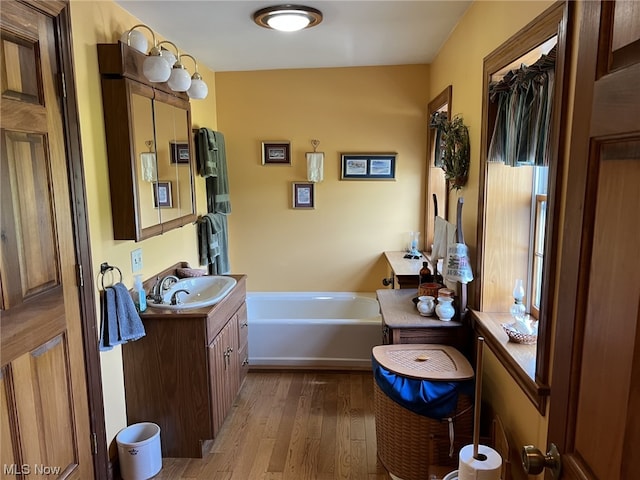 bathroom with hardwood / wood-style flooring, a tub to relax in, and vanity