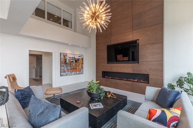 living room with wood walls, a notable chandelier, a tiled fireplace, and a towering ceiling