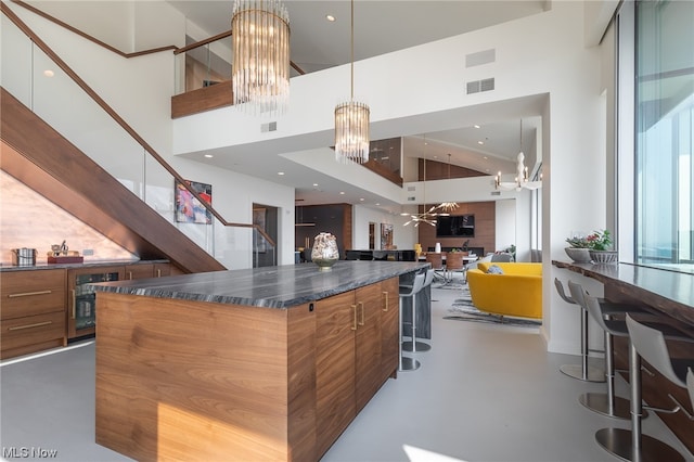 kitchen with dark stone counters, a kitchen island, hanging light fixtures, a high ceiling, and a breakfast bar