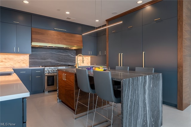 kitchen featuring a breakfast bar area, decorative backsplash, an island with sink, and wall chimney exhaust hood