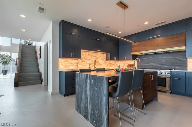 kitchen featuring decorative backsplash, a center island with sink, wall chimney range hood, a kitchen breakfast bar, and hanging light fixtures