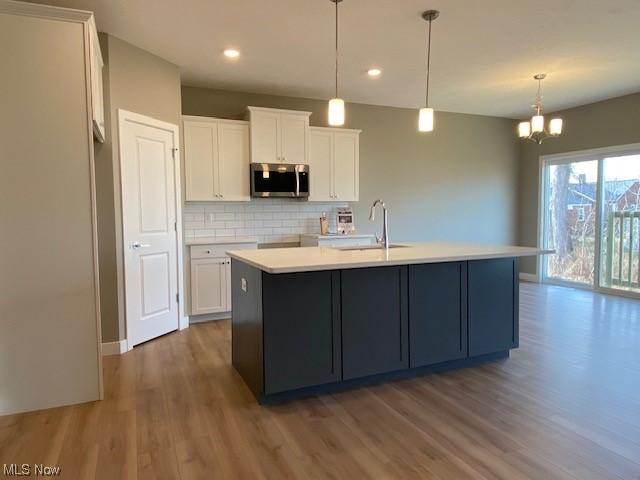 kitchen with white cabinets, a center island with sink, decorative backsplash, and hanging light fixtures