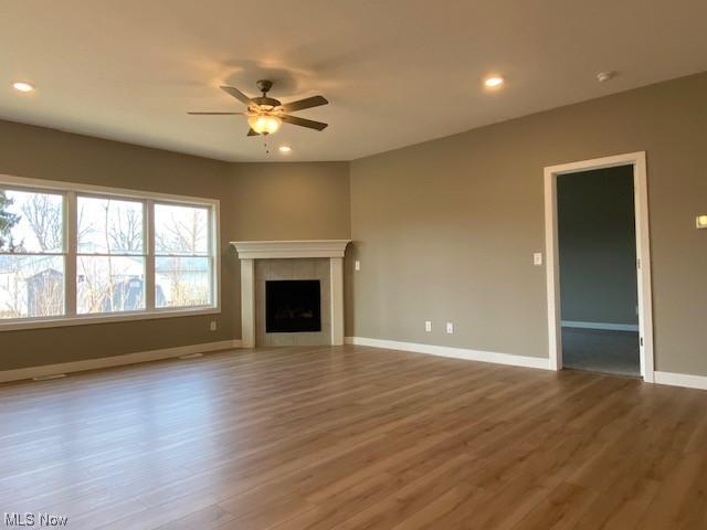 unfurnished living room with a tile fireplace, hardwood / wood-style floors, and ceiling fan