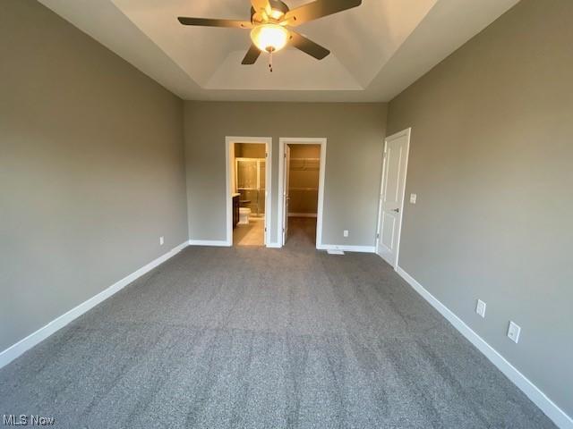 unfurnished bedroom with a walk in closet, ceiling fan, a tray ceiling, and a closet