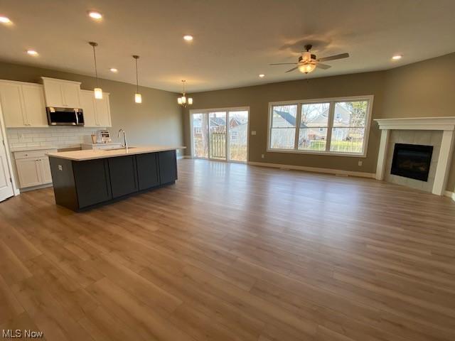 kitchen featuring pendant lighting, a kitchen island with sink, backsplash, ceiling fan with notable chandelier, and white cabinets