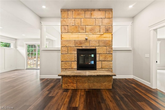 unfurnished living room with a stone fireplace and dark wood-type flooring