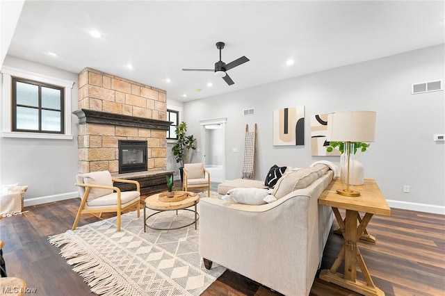 living room with a stone fireplace, ceiling fan, dark hardwood / wood-style flooring, and a healthy amount of sunlight