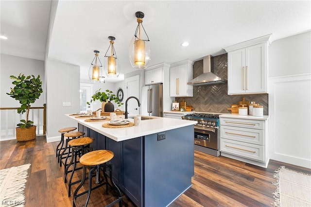 kitchen with wall chimney exhaust hood, pendant lighting, high quality appliances, white cabinets, and an island with sink