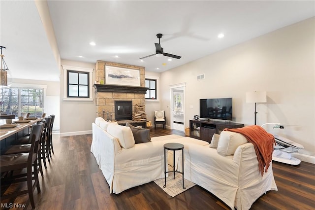 living room featuring a stone fireplace, ceiling fan, and dark wood-type flooring