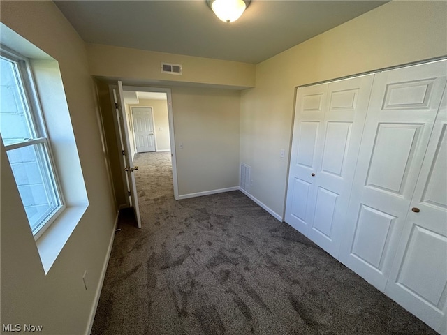 unfurnished bedroom featuring dark colored carpet, a closet, and multiple windows