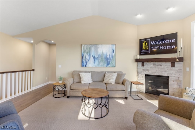 living room with light wood-type flooring, lofted ceiling, and a stone fireplace