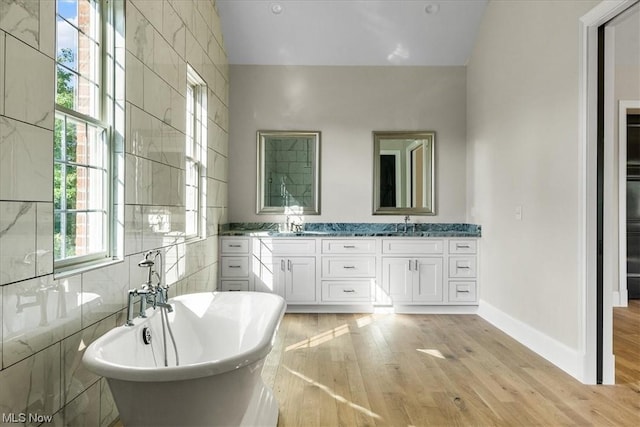 2585 Glendale Rd, Marietta, OH 45750 - full bathroom featuring wood finished floors, double vanity, a freestanding tub, a sink, and tile walls