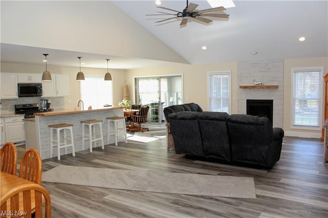 living room with dark wood-type flooring, sink, high vaulted ceiling, ceiling fan, and a fireplace