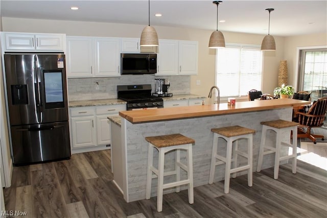 kitchen with appliances with stainless steel finishes, tasteful backsplash, an island with sink, white cabinets, and dark hardwood / wood-style flooring