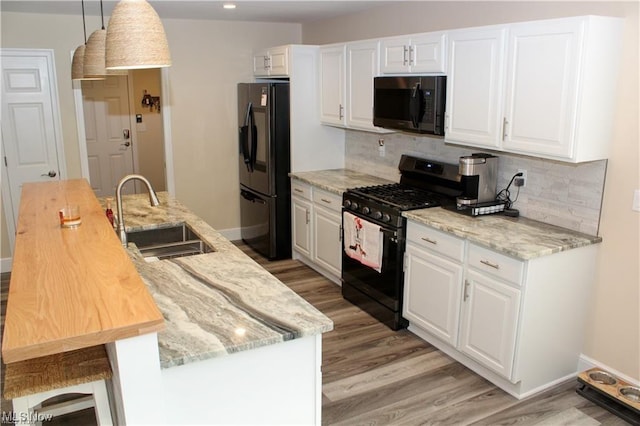 kitchen featuring sink, white cabinetry, black appliances, light stone countertops, and decorative light fixtures