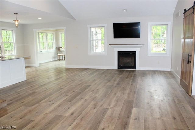 unfurnished living room with plenty of natural light, a barn door, and light wood-type flooring