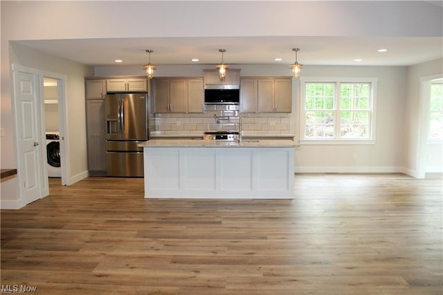 kitchen with decorative light fixtures, stainless steel fridge, washer / clothes dryer, light stone countertops, and decorative backsplash