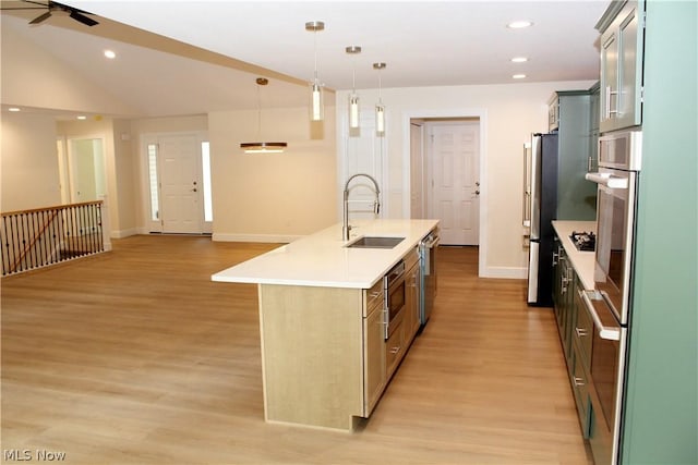 kitchen featuring appliances with stainless steel finishes, decorative light fixtures, sink, light hardwood / wood-style floors, and a center island with sink