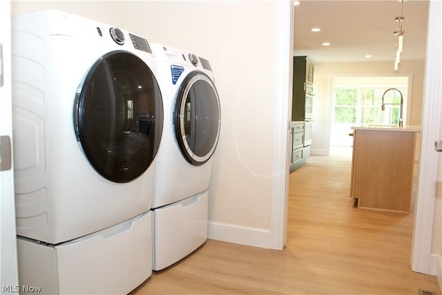 laundry area with sink, washer and clothes dryer, and light hardwood / wood-style floors