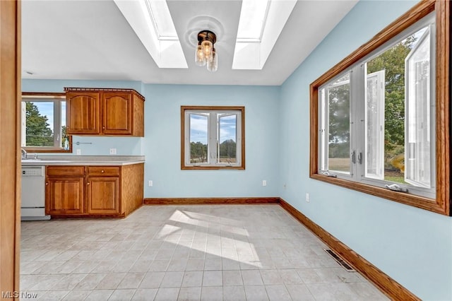 kitchen with a skylight, sink, light tile patterned floors, decorative light fixtures, and dishwasher