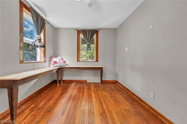 unfurnished office featuring wood-type flooring, built in desk, and plenty of natural light