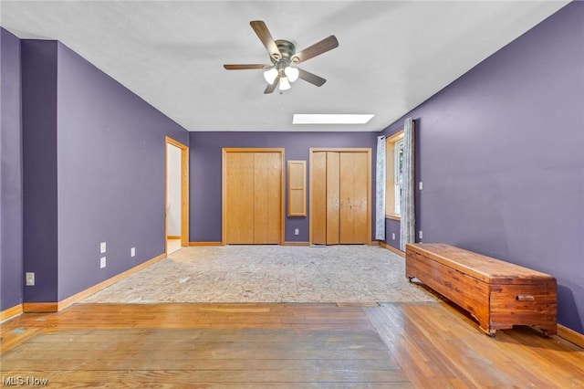 unfurnished bedroom featuring ceiling fan, two closets, light hardwood / wood-style flooring, and a skylight