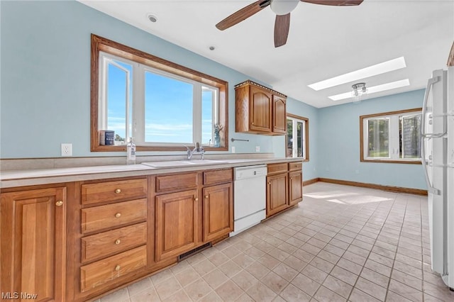 kitchen with a skylight, white appliances, ceiling fan, sink, and light tile patterned floors