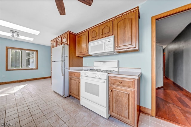 kitchen with a skylight, ceiling fan, light tile patterned floors, and white appliances