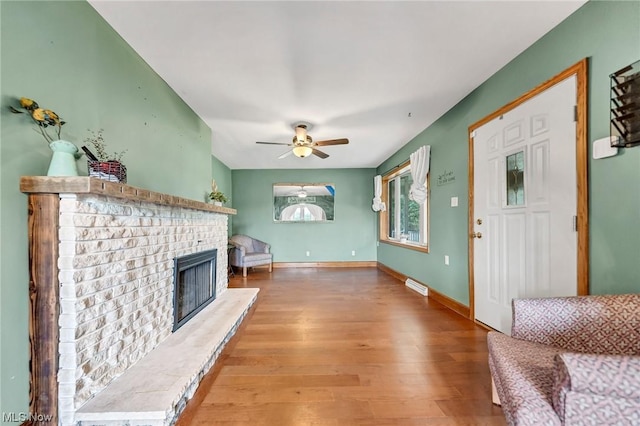 unfurnished living room featuring hardwood / wood-style flooring, ceiling fan, and a brick fireplace