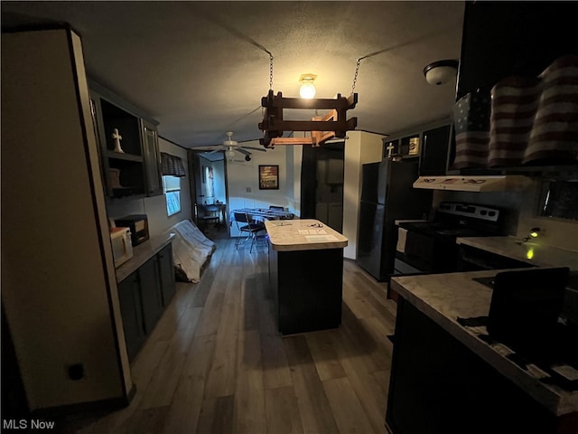 kitchen with a center island, ceiling fan, electric stove, black fridge, and hardwood / wood-style flooring