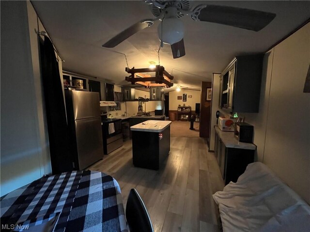 kitchen with a kitchen island, dark cabinets, freestanding refrigerator, light wood-style floors, and range with electric stovetop