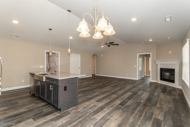 kitchen featuring hanging light fixtures, ceiling fan with notable chandelier, dark wood-type flooring, sink, and an island with sink