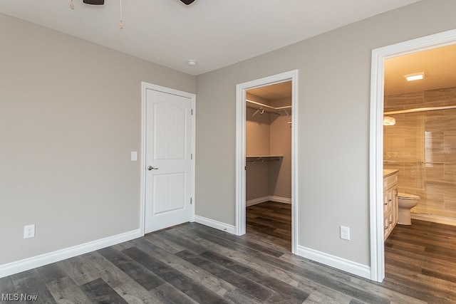 unfurnished bedroom featuring ensuite bath, a spacious closet, a closet, and dark wood-type flooring