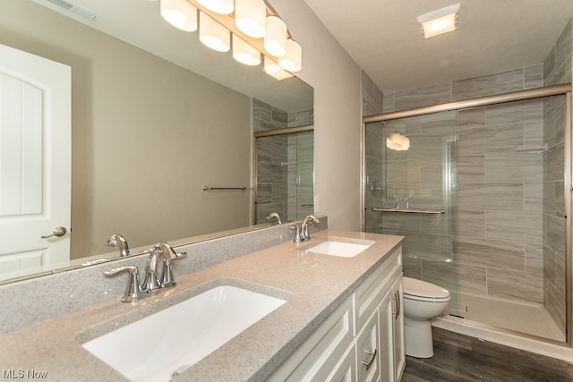 bathroom with a shower with shower door, double sink, toilet, hardwood / wood-style flooring, and vanity with extensive cabinet space