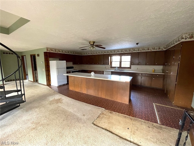 kitchen featuring white refrigerator, ceiling fan, a kitchen island, dark brown cabinetry, and a textured ceiling