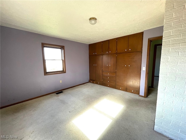 unfurnished bedroom with brick wall, a textured ceiling, and light colored carpet