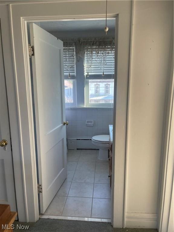 bathroom featuring a baseboard heating unit, tile patterned floors, toilet, vanity, and tile walls