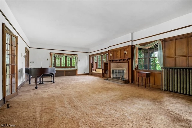 unfurnished living room with a healthy amount of sunlight, a brick fireplace, radiator, and carpet floors