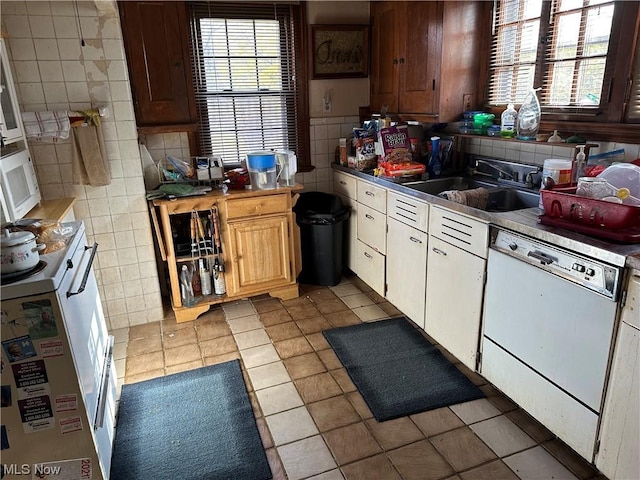 kitchen with white dishwasher, white cabinets, sink, and tile walls