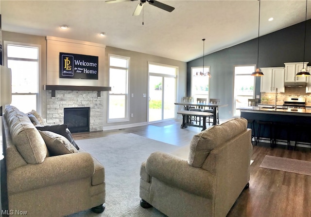 living room with a fireplace, dark wood-type flooring, a ceiling fan, vaulted ceiling, and baseboards