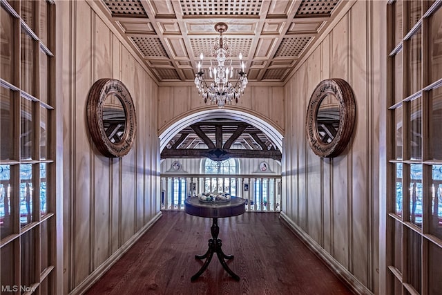 corridor featuring dark wood-type flooring, coffered ceiling, wooden walls, and a notable chandelier