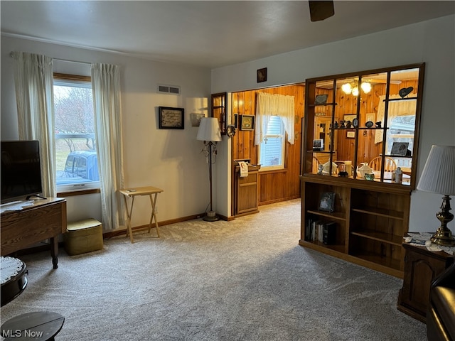 living area with ceiling fan, wooden walls, and carpet floors