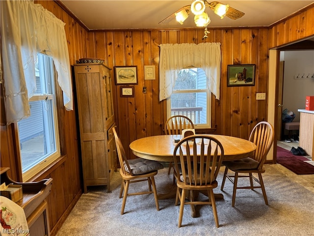 carpeted dining space with ceiling fan, ornamental molding, and wooden walls