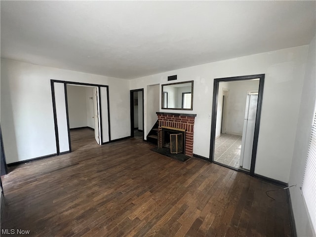 unfurnished living room featuring dark wood-type flooring and a brick fireplace