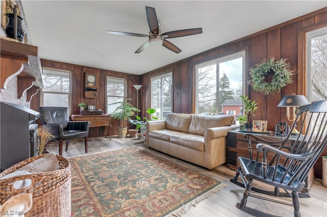 living room with light wood-type flooring, wooden walls, a wealth of natural light, and ceiling fan