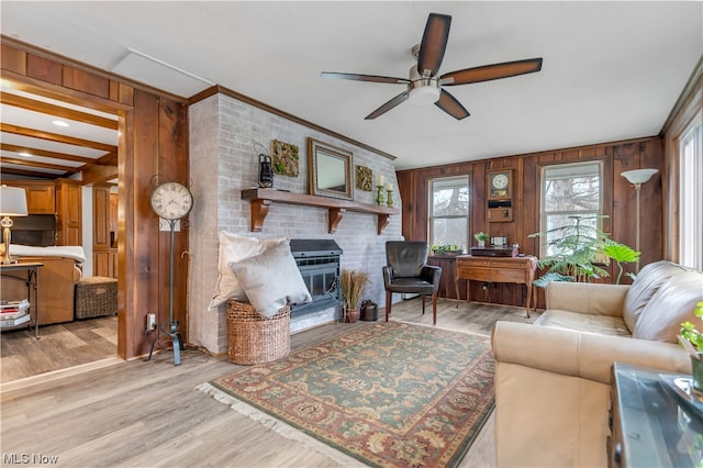 living room with wooden walls, crown molding, light wood-type flooring, and ceiling fan